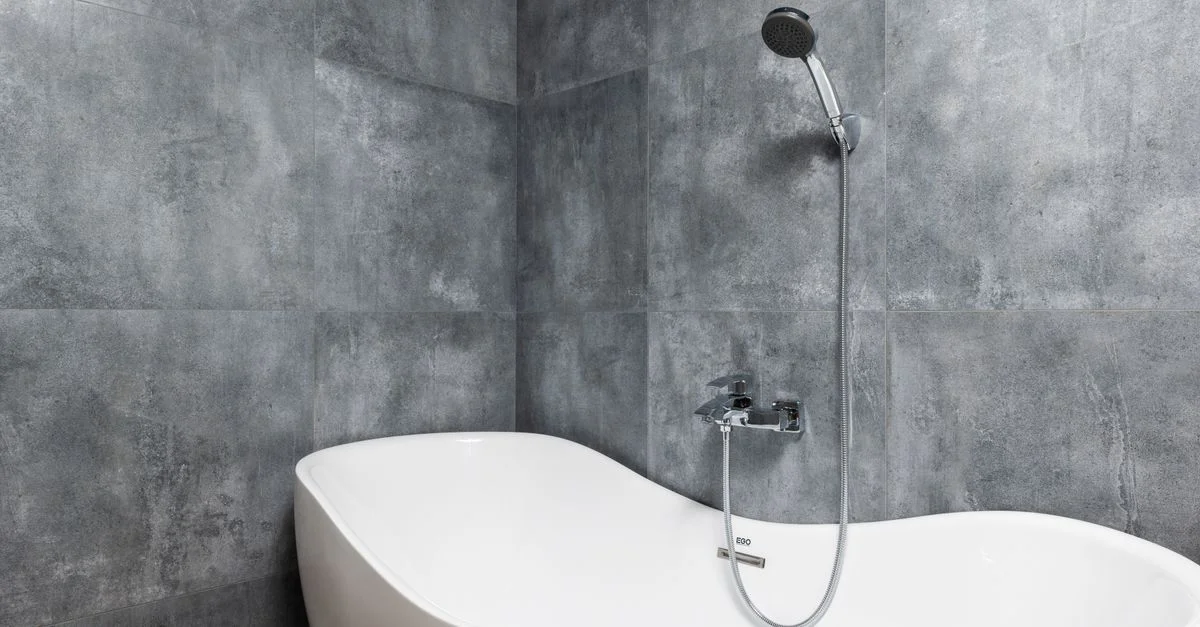 Élégante baignoire blanche dans une salle de bain moderne aux murs carrelés gris, avec un design épuré et une ambiance luxueuse.