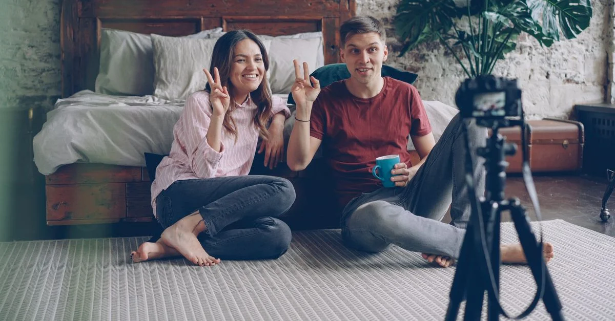Couple heureux assis par terre en train d'enregistrer un vlog dans une chambre confortable.